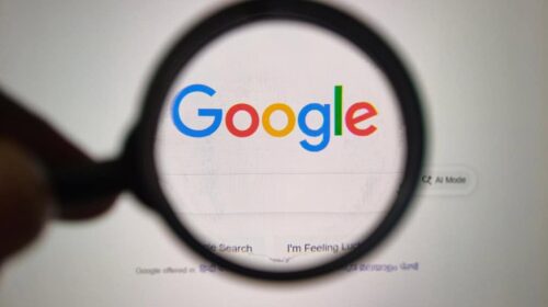 Um close-up de uma lente de aumento segurada sobre o logotipo icônico do Google exibido em um monitor de computador, destacando o poder da pesquisa.