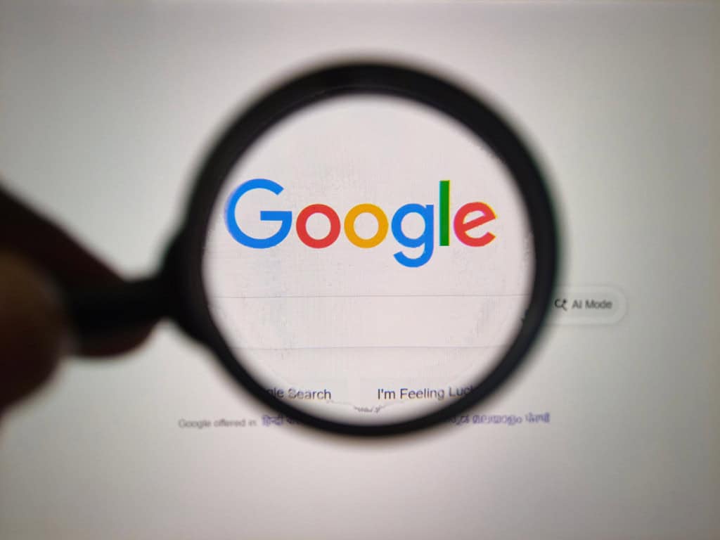 Um close-up de uma lente de aumento segurada sobre o logotipo icônico do Google exibido em um monitor de computador, destacando o poder da pesquisa.