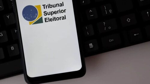 Logotipo do Tribunal Superior Eleitoral (TSE) exibido na tela de um smartphone sobre um teclado de computador.